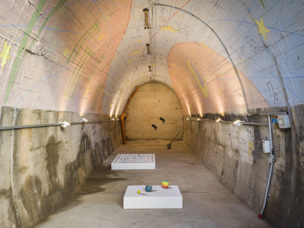 Installation view of different art works in an abbandoned tunnel with a painted ceiling.