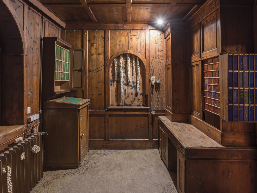 Installation view of an old hotel porters office with wood objects and paintings installed.