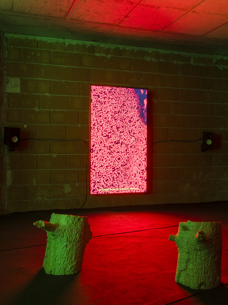 Installation view showing a video installation and wood stools arranged in a dark exhibition space.