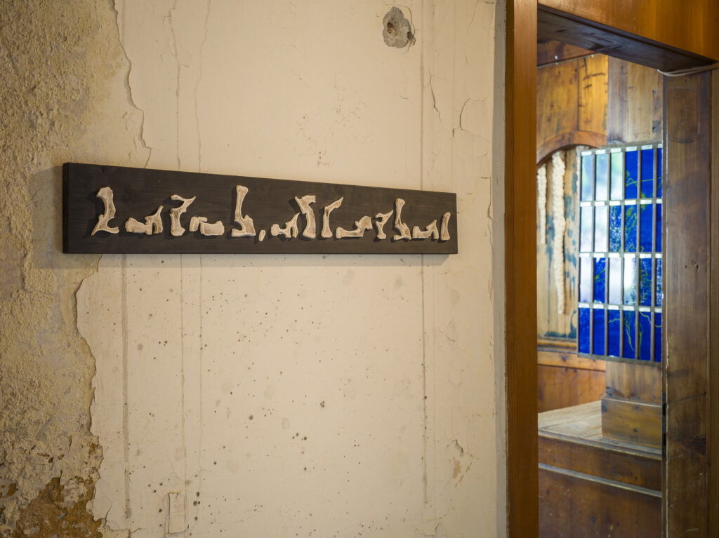 Installation view of an old hotel porters office with wood objects and paintings installed.