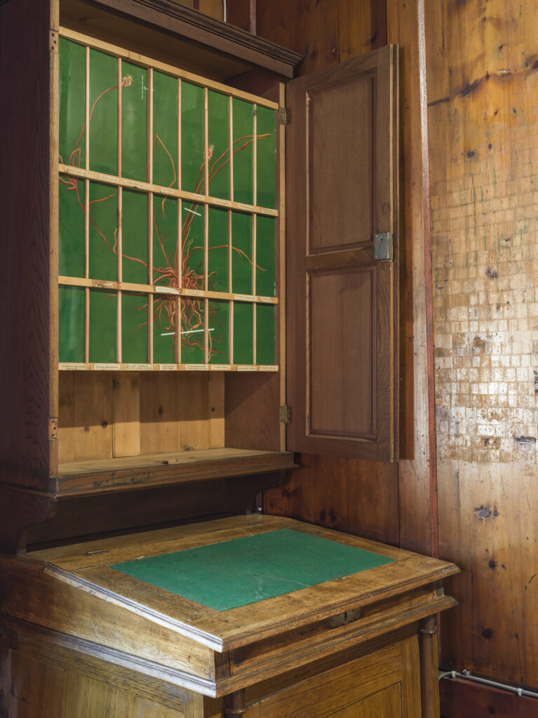 Installation view of an old hotel porters office with wood objects and paintings installed.