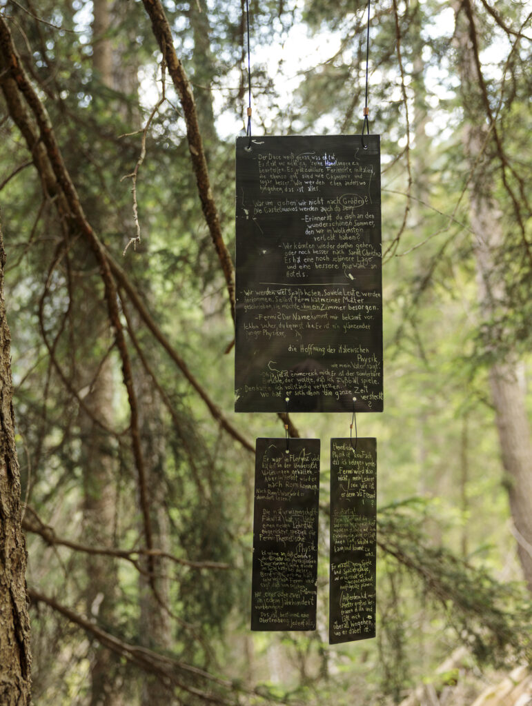 Installation view of the art work composed of inscripted, painted glass shards hanging from trees in the forest.