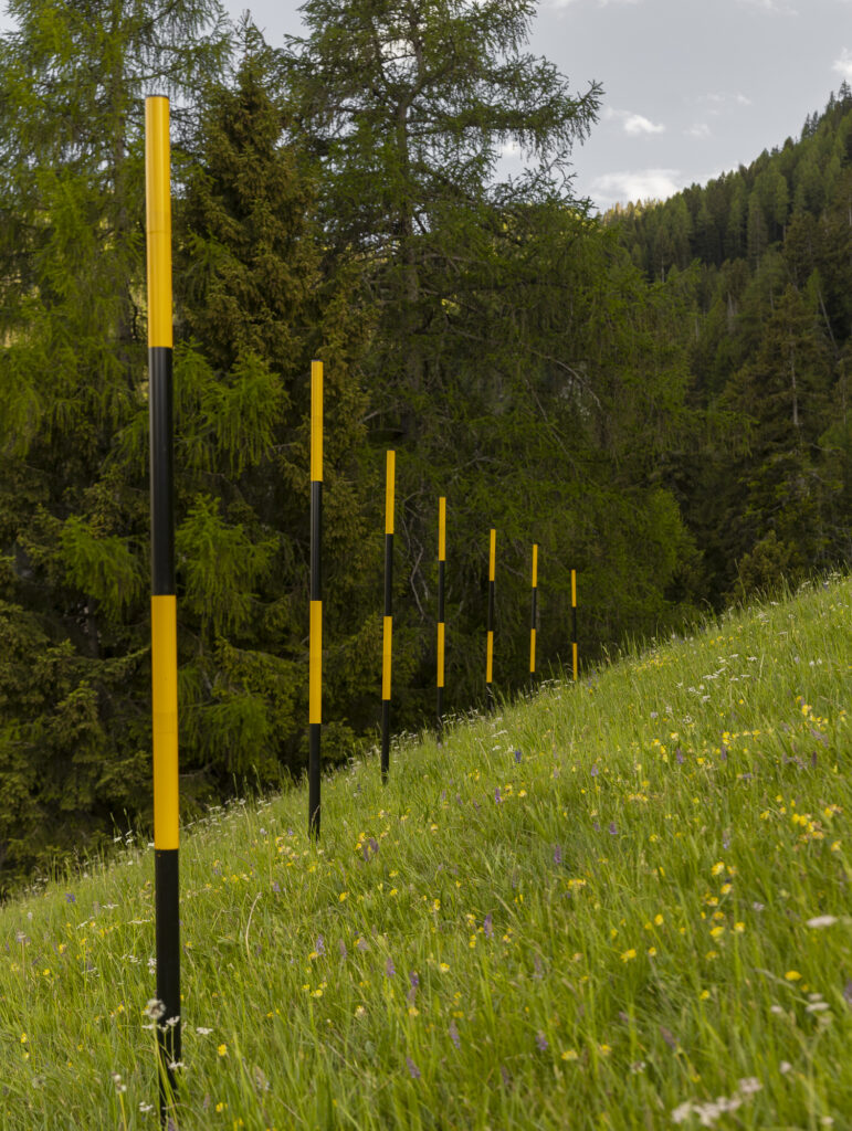 Installation view snow stakes in lines on a green mountain pasture.